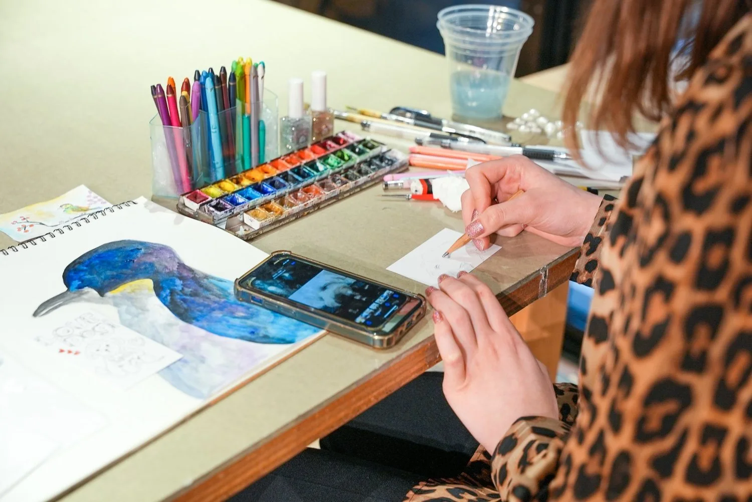 Hodokeruで色鉛筆と絵の具が並ぶテーブルで、紙に絵を描く手元